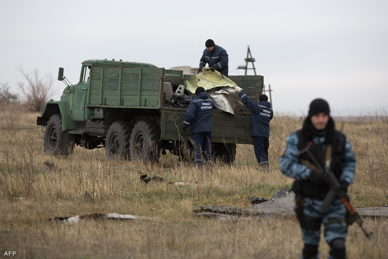 A donyecki önvédelmi erők emberei szállítják el a lelőtt gép roncsait, miközben oroszpárti fegyveresek biztosítják a területet.