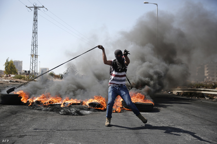 Palesztin tüntető kővel dobálja az izraeli fegyvereseket 2015. október 11-én Ramallah északi részén.