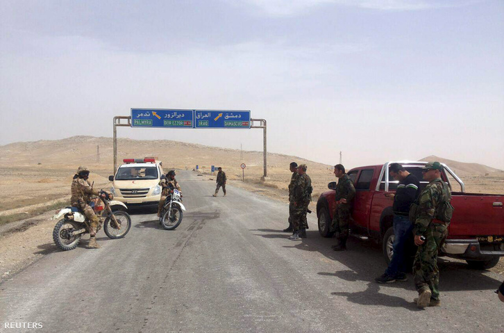 Szíriai kormányerők egy ellenőrzőpontnál, a háttérben a táblák a Palmüra felé vezető utat jelölik a híres romok közelében.