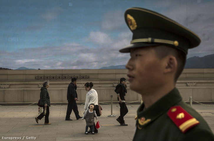 Turisták a Tiananmen téren, egy ledfalon vetített kék ég előtt.