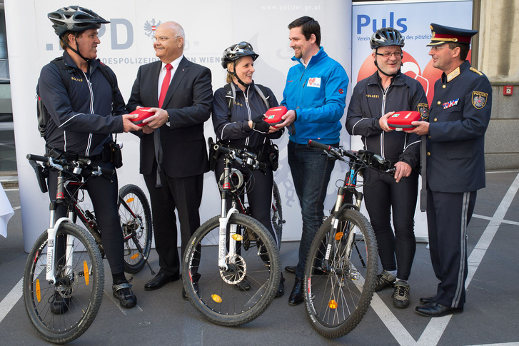 Harry Kopietz, a tartományi parlament elnöke, Gerhard Pürstl, a tartományi rendőrség vezetője és Markus Winnisch, a Puls Egyesület projektvezetője adja át a mini-defibrillátorokat a Bécsi Rendőrség biciklis járőreinek.