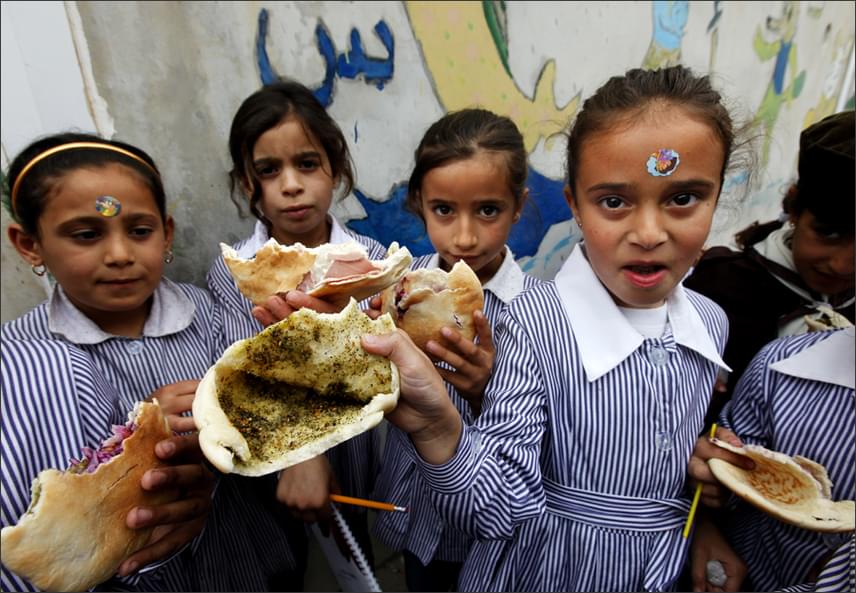 
                        	Olajjal kevert fűszerrel megkent pitát esznek ebédre ezek a palesztin kislányok, csak a szerencsésebbeknek jutott némi zöldség vagy egy szelet felvágott a vékonyka szendvicsbe. A Nablus városában található intézményben nincs iskolai étkeztetés, mindenki otthonról viszi a harapnivalót, ami sajnos gyakorta nem túl tápláló, és nem is túl laktató.
