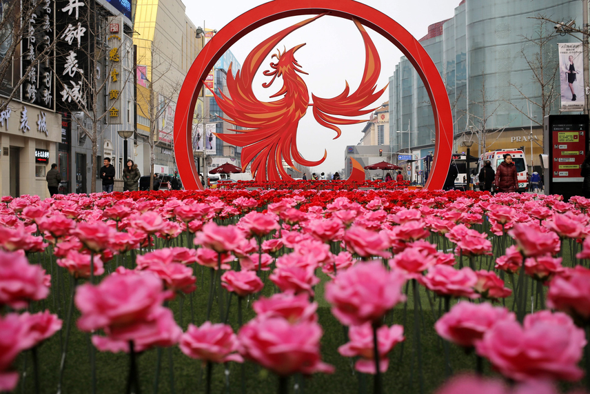 
                        	Műanyag virágok egy óriási kakasdekoráció tövében a holdújév alkalmából Pekingben. A kínai holdnaptár szerint január 28-án köszönt be az új év, amely az állatövek szerint jelölt 12 esztendő közül a kakas éve lesz.