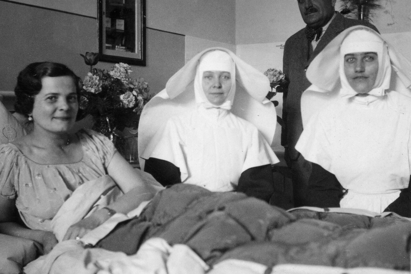 1938-ban így nézett ki egy hölgybeteg az ápolói és családja körében. A falba beugró kis szekrényben kedvenc tárgyai vannak, az ágyon az otthoni tükrös paplan szolgáltatja a kényelmet.