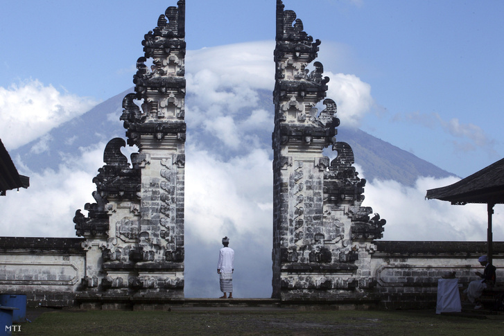 A felhőkbe burkolózott Agung tűzhányót nézi egy indonéz férfi egy templomkerítés kőcsipkéi közt a Bali-szigeti Karangasemben 2017. szeptember 26-án
