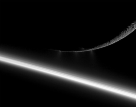 A világűrbe jutva apró jégdarabok áramává fagyó vízkitörés a Szaturnusz éjszakai oldala előtt tartózkodó Enceladus hold déli pólusánál. A kép alján lévő, fényes ív a gyűrűs bolygó légköre felett átszüremlő napfény (NASA/JPL/Space Science Institute).