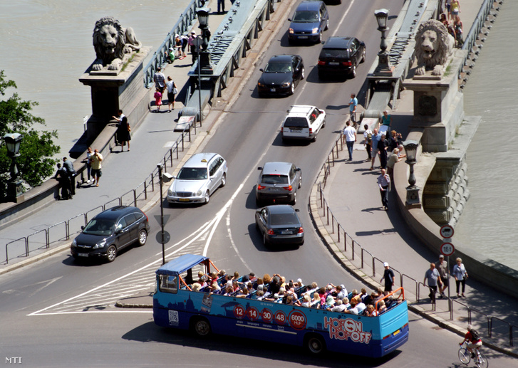 Városnéző turistákat szállító nyitott Hop On Hop Off autóbusz halad el a Széchenyi Lánchíd budai hídfőjénél a Clark Ádám téren.