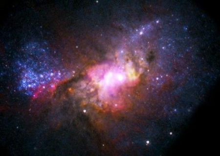 A Henize 2-10 katalógusjelű törpegalaxis kompozit képe. A Hubble Űrteleszkóp felvételét vörös, zöld és kék színek, a VLA rádióadatait sárga, míg a Chandra röntgenméréseit bíbor színek kódolják. [Reines és tsai, NRAO/AUI/NSF, NASA]