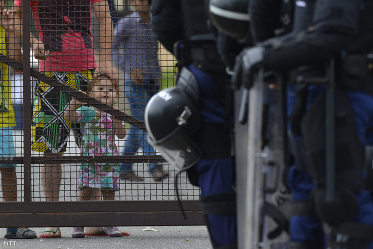 A debreceni migrációs tábor lakói nézik a tábor bejáratánál felsorakozó rendőröket 2015. június 29-én.