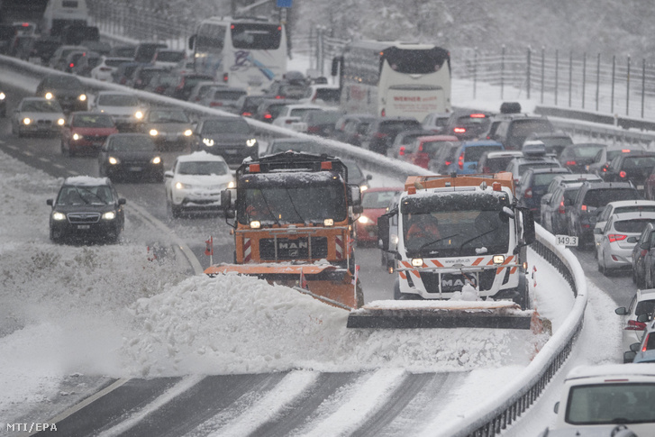Hókotrók takarítják az autópályát a hóesésben araszoló autóoszlop előtt a Gotthard-alagútnál a svájci Erstfeld közelében 2018. március 31-én.