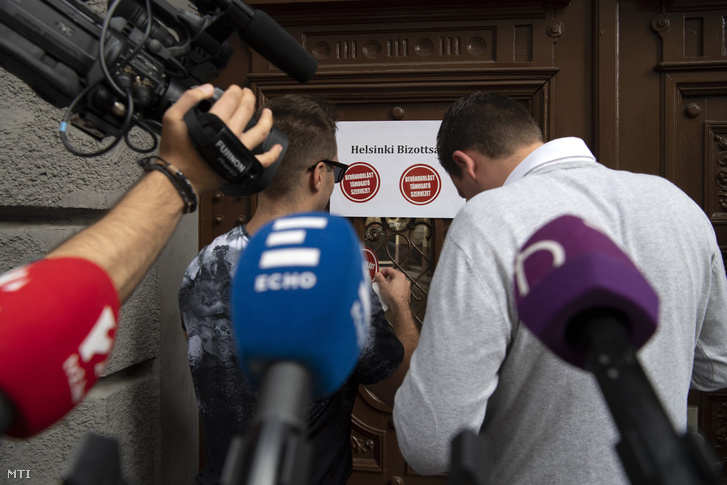 „Bevándorlást támogató szervezet” feliratú matricákat ragasztanak a bejárathoz a kormánypárt ifjúsági társszervezete, a Fidelitas aktivistái a Magyar Helsinki Bizottság irodájának helyet adó épület előtt tartott sajtótájékoztatón Budapesten 2018. június 27-én.