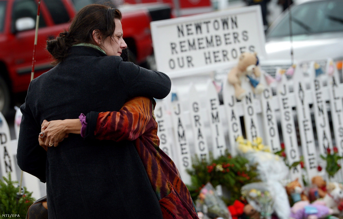 Gyászoló nők ölelik egymást a tragédia gyerekáldozatainak nevével teleírt kerítés előtt a Connecticut állambeli Newtownban 2012. december 21-én. Egy héttel korábban a húsz éves Adam Lanza agyonlőtt 26 embert, köztük 20 kisgyereket a newtoni Sandy Hook általános iskolában. A táblán olvasható felirat jelentése: "Newtown emlékszik a hőseinkre".