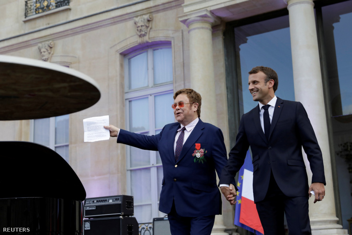 Emmanuel Macron francia elnök és Elton John kézen fogva jönnek ki az Elysée-palota udvarára 2019. június 21-én.