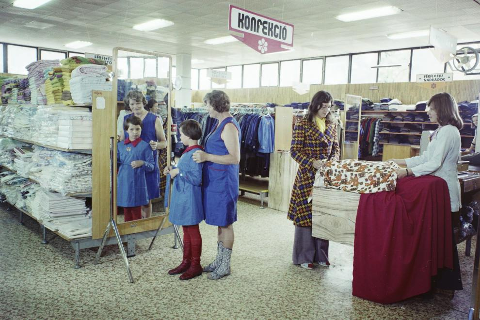 Az iskolaköpeny akkoriban még kötelező volt, egyfajta egyenruhaként, ám többféle fazon is létezett. A gödöllői, Szabadság téri áruházban így próbálta új köpenyét egy kislány 1974-ben.