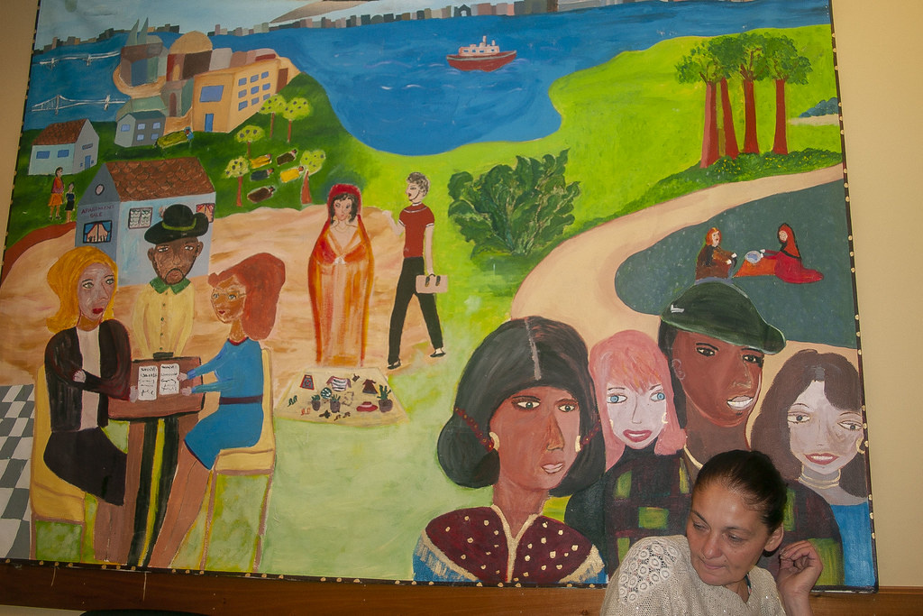 A CultureLink és a Roma Community Center közös irodájának várakozóterét díszíti egy falfestmény, amit hét magyar roma asszony készített néhány éve, és ami a kivándorlások történeteit ábrázolja. A bal sarokban épp egy szerződést aláírása látható. A magyarországi otthonaikat adják el a kivándorlásra készülő cigányok, felszámolva mindent maguk után.