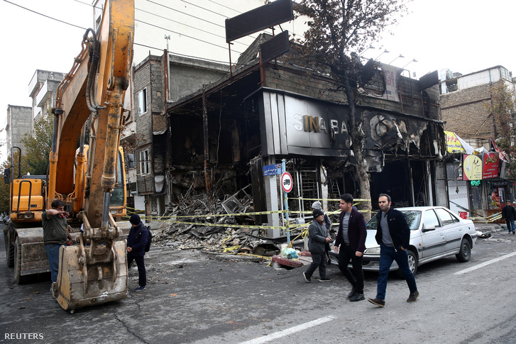 Felgyújtott bank épülete mellett sétálnak a járókelők Teheránban 2019. november 20-án