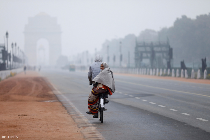 Nő ül a bicikli hátulján a mai hideg téli reggelen Új-Delhiben