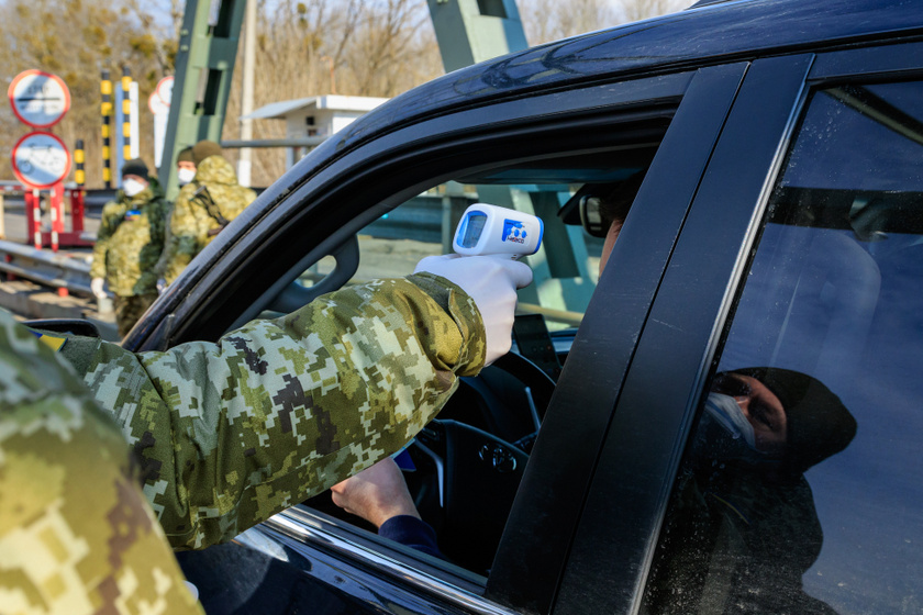 Ukrán határőr méri egy hazafelé érkező gépkocsivezető testhőmérsékletét az ukrán-magyar határon.