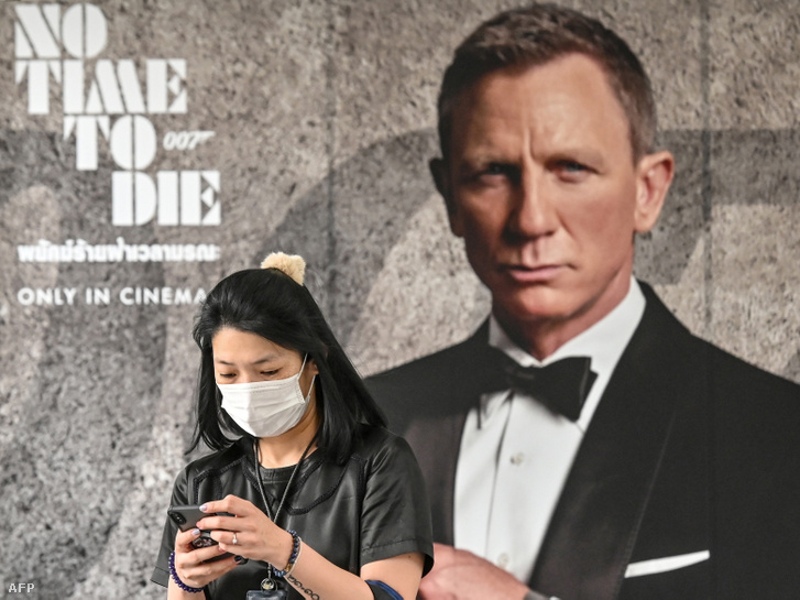 Nő sétál úúj James Bond plakát előtt maszkban a koronavírus miatt Bangkokban 2020. február 28-án