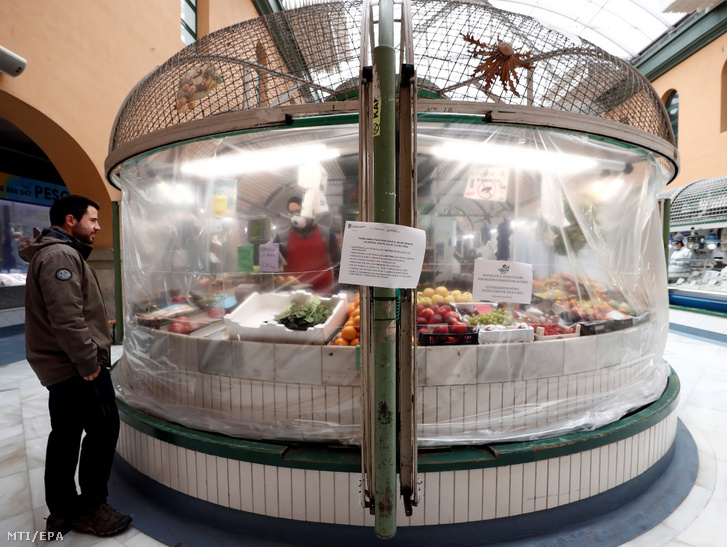 Műanyag védősátor alól szolgálja ki vásárlóit egy zöldség-gyümölcs kereskedő Pamplonában 2020. március 18-án