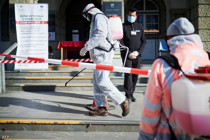 Védőruházatba öltözött munkások fertőtlenítik az utcát a városháza előtt a szlovéniai Kranjban 2020. március 23-án