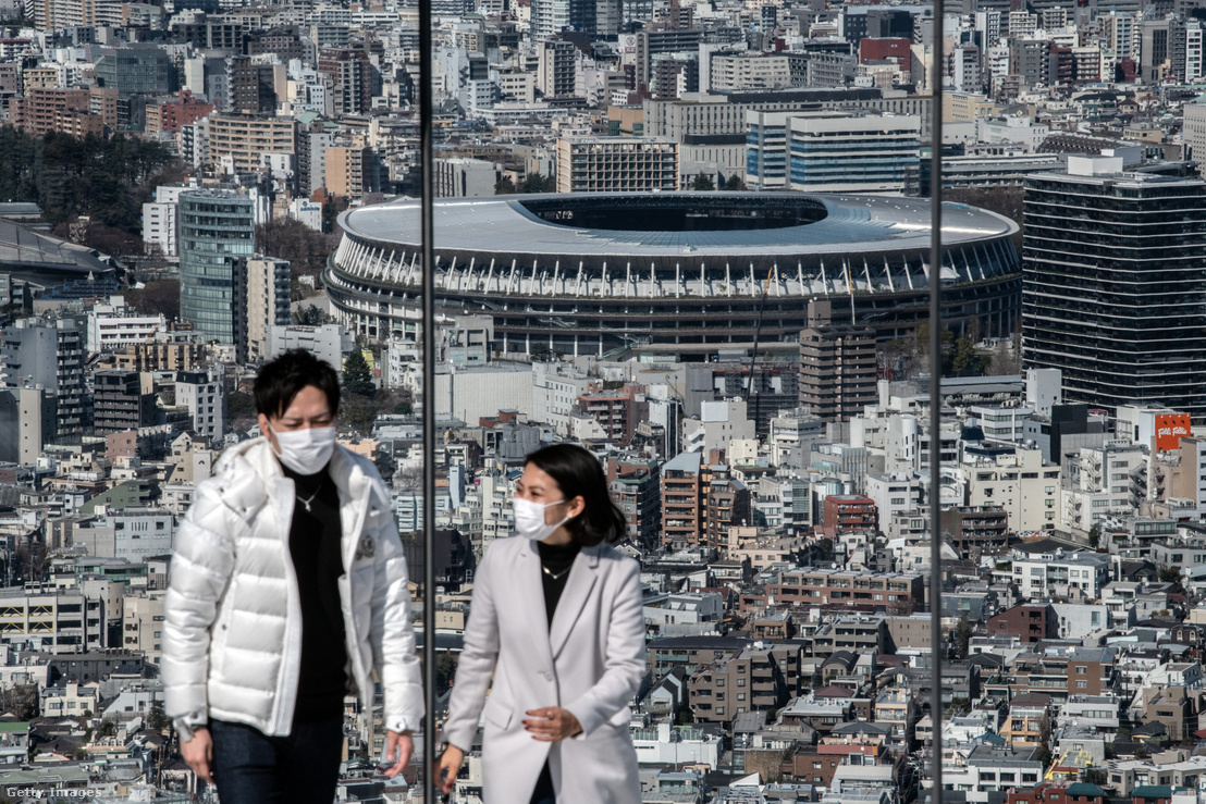 Maszkot viselő emberek egy tokiói kilátóteraszon, háttérben az Olimpiai Stadion