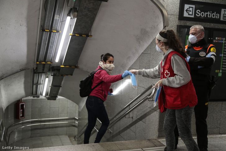 Egy utas maszkot kap a Vöröskereszt munkatársától a barcelonai metró Passeig de Gracia állomásánál