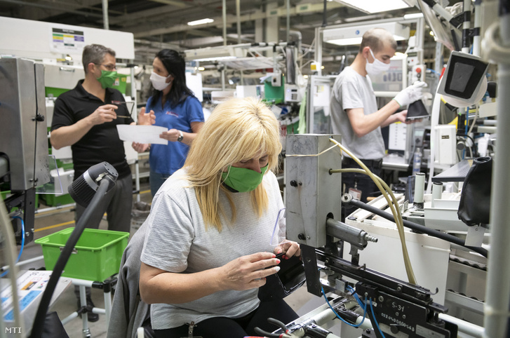 Szájmaszkot viselő dolgozók sebességváltókar-burkolatokat készítenek az autóipari alkatrészeket gyártó Eissmann Automotive Hungária Kft. gyárában Nyíregyházán 2020. március 27-én