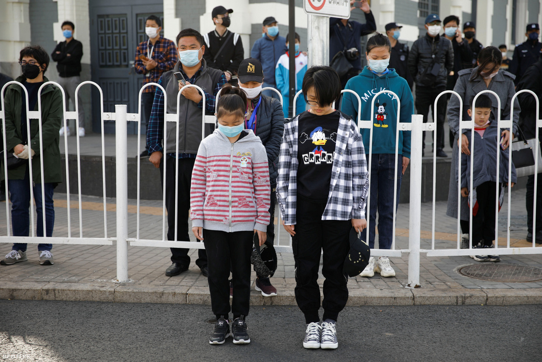 Arcmaszkot viselő emberek állnak lehajtott fejjel az utcán Pekingben 2020. április 4-én. Helyi idő szerint délelőtt tízkor az egész országban megállt az élet három percre, hogy a járványban elhunytakra, különösen a koronavírus megállításáért életüket adó egészségügyi dolgozókra emlékezzen.