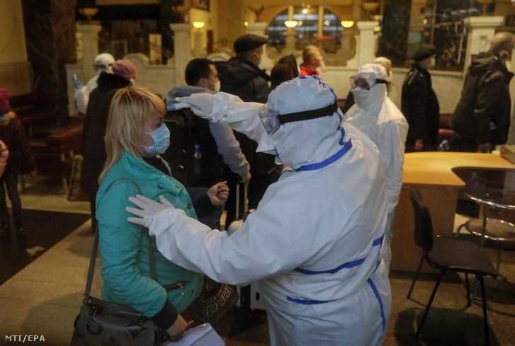 Egészségügyi dolgozó ellenőrzi egy felszállásra várakozó utas testhőmérsékletét a kijevi vasútállomáson