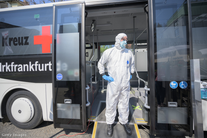 Koronavírus tesztelésre specializált autó ajtajában áll egy alkalmazott, hogy az idősotthonok lakóit széles körben teszteljék Frankfurtban 2020. április 8-án.