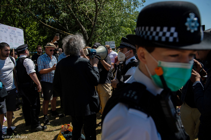 Szájmaszkos rendőr a londoni Hyde parkba szervezett, korlátozás-ellenes tüntetésen, amelyen épp Piers Corbyn, a Munkáspárt korábbi vezetője, Jeremy Corbyn testvére szólal fel
