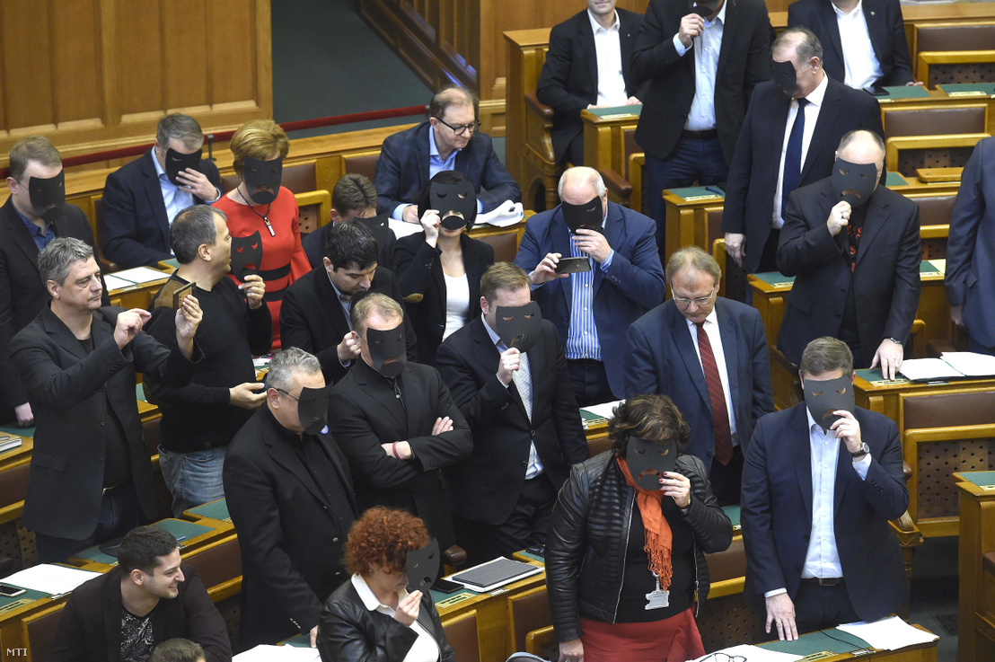 A DK és az MSZP képviselői a kulturális törvénycsomag szavazása közben tiltakozásul felállnak és fekete maszkot tartanak az arcuk elé az Országgyűlés plenáris ülésén 2019. december 11-én. A kormánypárt kommunikációja szerint a törvénymódosítást a Katona József Színház zaklatási ügye tette indokolttá.