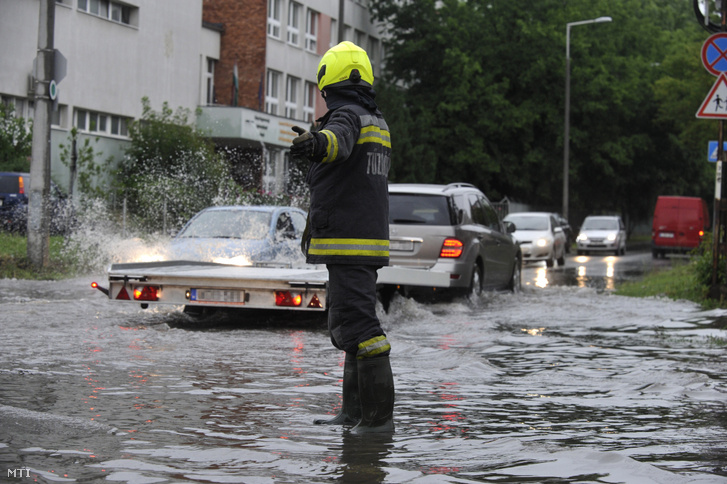 Tűzoltó irányítja a vihar után összegyűlt esővízben haladó járműveket a főváros X. kerületében a Maglódi út és a Gitár utca kereszteződésénél 2020. június 14-én