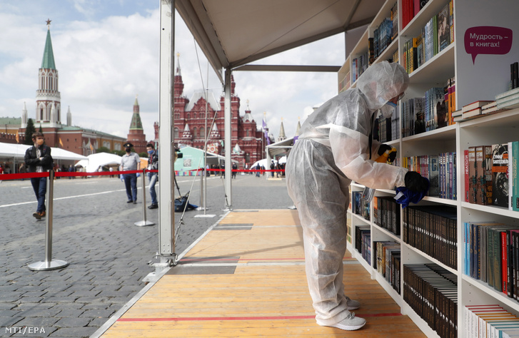 Könyvespolcot fertőtlenít egy védőruhát viselő egészségügyi dolgozó a moszkvai Vörös téren nyílt könyvvásáron 2020. június 6-án.