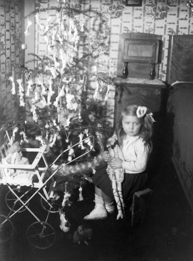 Kislány ajándékokkal egy szaloncukrokkal díszített fa alatt 1909 karácsonyán