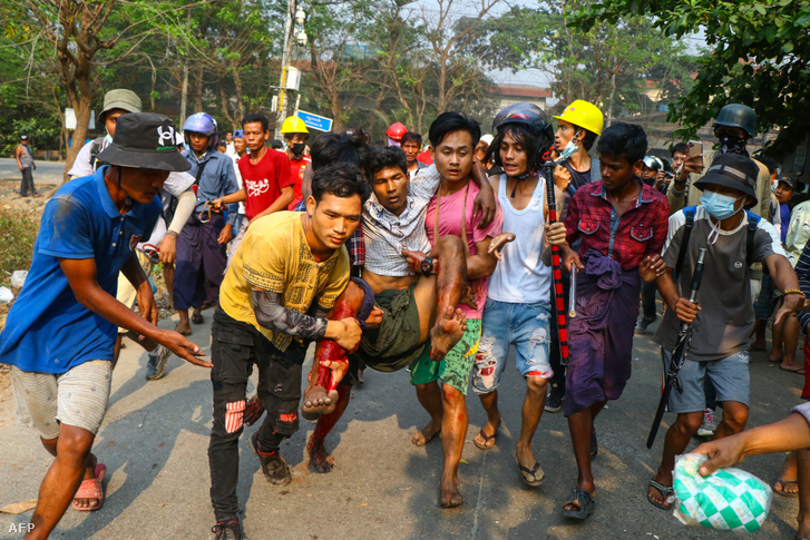 Egy férfit cipelnek biztonságos helyre Yangonban miután megsérült a tüntetésen 2021. március 14-én