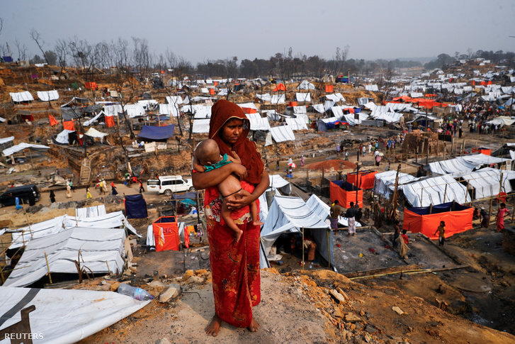 Egy rohingja menekült nő gyermekét tartja kezében, miközben körül tekint a porig égett menekülttábor helyén.
