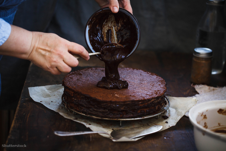 Egy cukrász csokoládéganassal vonja be a tortát