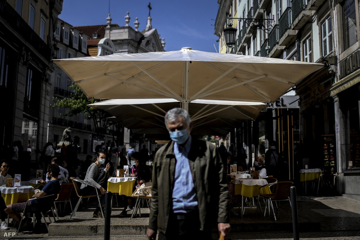 Egy férfi elsétál a kávézó teraszán ülő emberek mellett a lisszaboni Chiado városnegyedben 2021. április 5-én