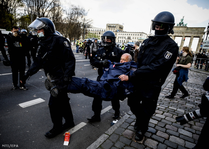 A koronavírus-járvány megfékezését célzó kormánypolitika ellen tüntetők egyikét veszik őrizetbe rohamrendőrök Berlinben 2021. április 21-én