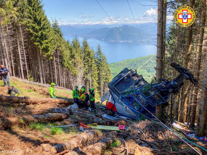 Az olasz nemzeti hegyimentő szolgálat (CNSAS) által közreadott kép mentőcsapat tagjairól az észak-olaszországi Stresa települése és a Mottarone-hegy között közlekedő függővasút egyik lezuhant fülkéje mellett Verbania közelében 2021. május 23-án.