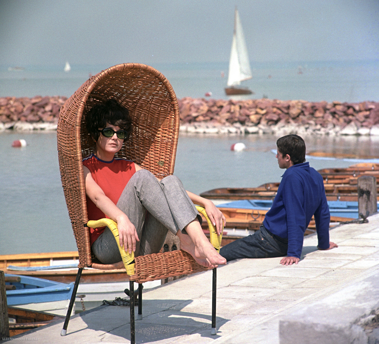 1968. június 18. Vellai Zsuzsanna modell fonott kerti bútort reklámoz egy balatoni településen a tóparton az Artex Külkereskedelmi Vállalat megrendelésére készült felvételen. A felvétel készítésének pontos helye ismeretlen