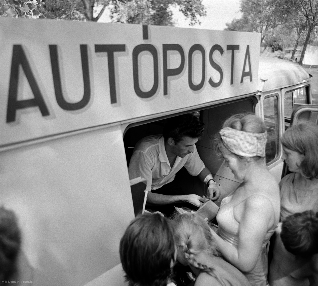 1965. július 21. Leveleket adnak fel egy kempingben nyaralók a Magyar Posta új, kelet-német gyártmányú, Barkas B1000 típusú kis teherjárművében működő, mozgó postahivatalánál. Az úgynevezett autóposta a balatoni kempingezők eddigi levelezési gondjain segít. A jármű mindennap meglátogatja a lakott területektől távol eső sátortáborokat, és gondoskodik arról, hogy a nyaralók üdvözlőlapjai késedelem nélkül eljuthassanak a címzettekhez. Az autóposta magyar és külföldi kiadású újságokat és képeslapokat is árusít. A felvétel készítésének pontos helye ismeretlen