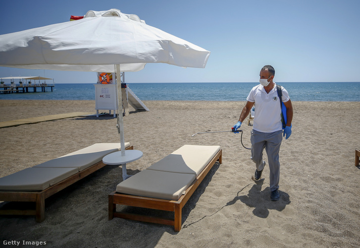 Védőmaszkot viselő alkalmazott fertőtleníti a napozóágyakat egy szálloda strandján a törökországi Antalyában 2020. július 3-án