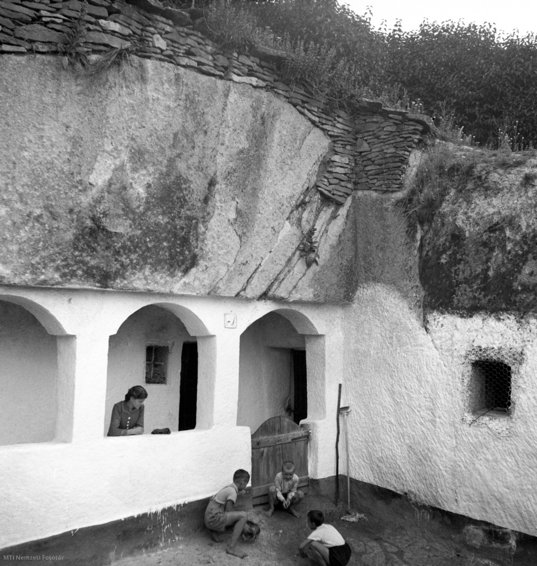 Szomolya, 1955. július 14.  Kása Gábor földműves gyermekei barlanglakásuk előtt játszanak. A Falusi Lakásépítési Gazdasági Iroda (Fagi) egy- és kétszobás kislakások építését kezdte meg 1954 tavaszán a faluban