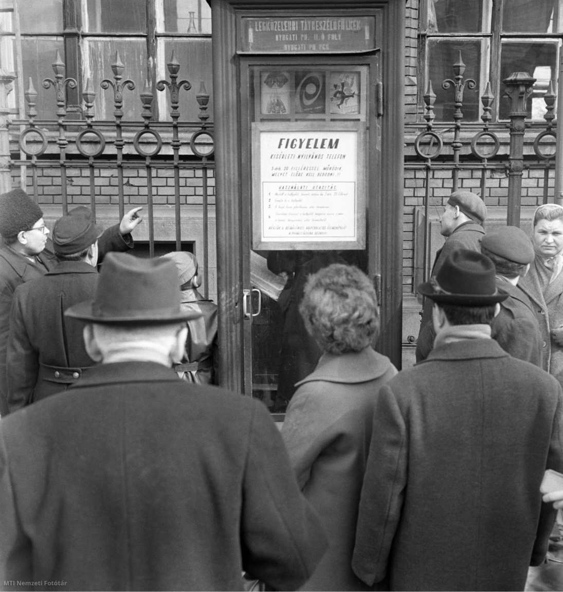 Járókelők nézik a Nyugati pályaudvarnál felszerelt kísérleti telefonfülkét 1964 májusában. Ehhez a típushoz nem kell telefonérme, hanem három darab húszfilléres bedobásával működik