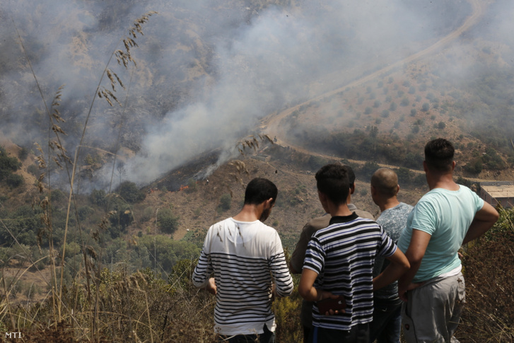 Helyi lakosok nézik az algériai Toudja falu közelében pusztító erdőtűz lángjait 2021. augusztus 13-án