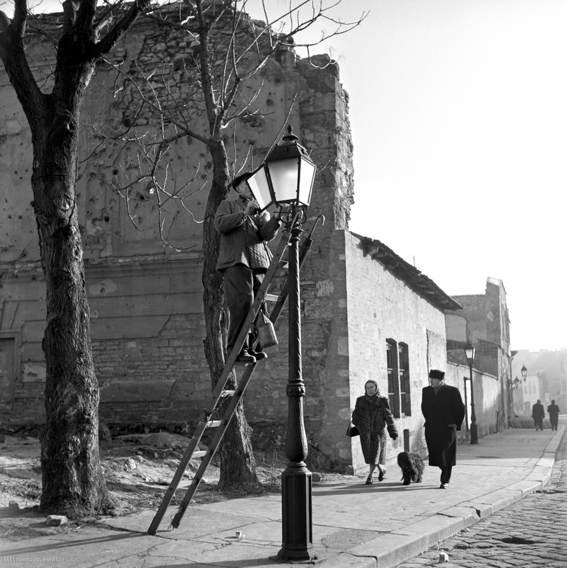 Budapest, 1958. január 3. Lámpagyújtó szakember ellenőrzi a gázlámpát a budai Várban. Pesten és Budán először 1816-ban világítottak gázzal. Az első lámpát Tehel Lajos, a Nemzeti Múzeum természettárának őre az akkori múzeumépület homlokzata előtt gyújtotta be. 1856. december 21-én a petróleumlámpák használatával egy időben a Kerepesi (mai Rákóczi) úton kigyulladtak a főváros első közvilágítási gázlámpái. A II. világháborúban a közvilágítási rendszer jelentős hányada megsemmisült vagy megrongálódott, a károk helyreállítása 1949-ig tartott. A hatanas évek végére a gázvilágítás gyakorlatilag megszűnt, egyeduralkodóvá vált az elektromos közvilágítás. Működő gázlámpák vannak még a budai Várban, a Margitszigeten és a Gázművek Köztársaság téri múzeuma előtt
