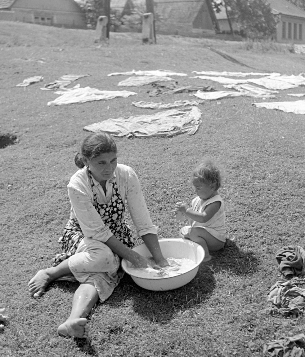 Dömsöd, 1957. június 24. Egy anya lavórban mos a holt Duna-ágnál Dömsödnél, mellette gyermeke játszik. Háttérben a fűre teregetett ruhák száradnak.